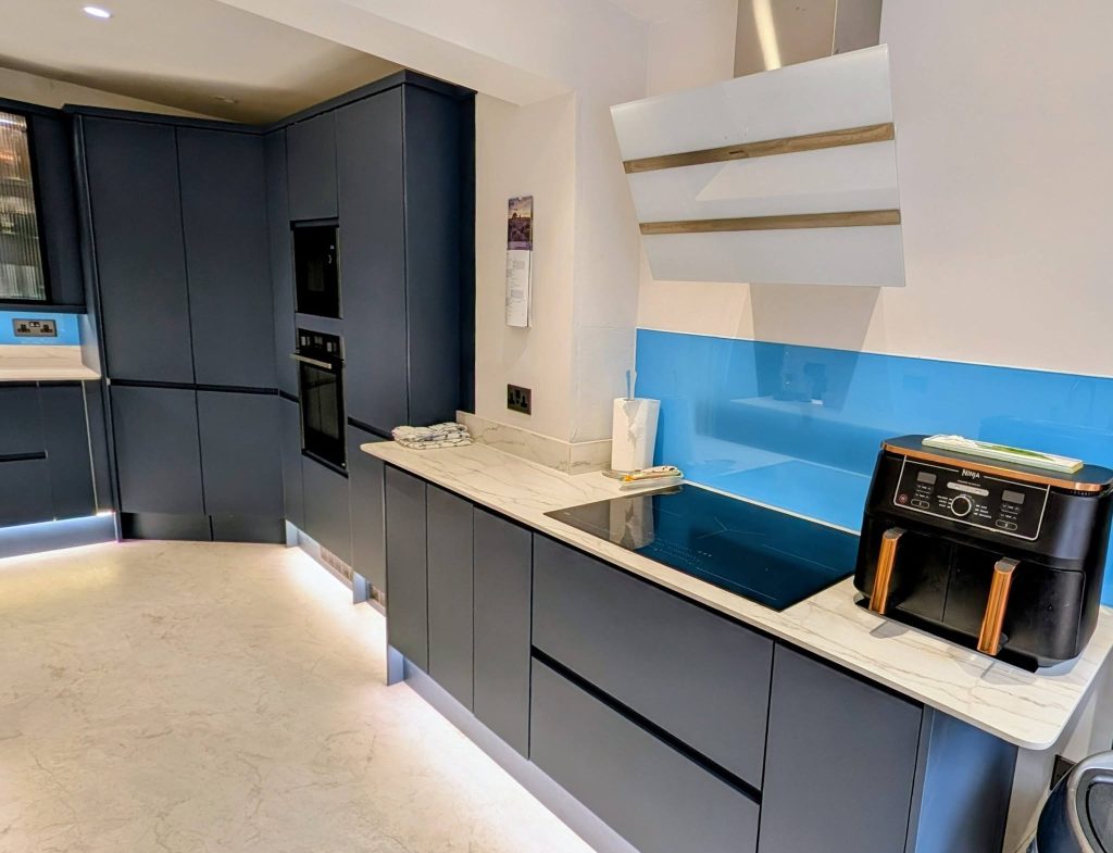 Blue handleless kitchen with white worktops, an induction hob and white splashback.