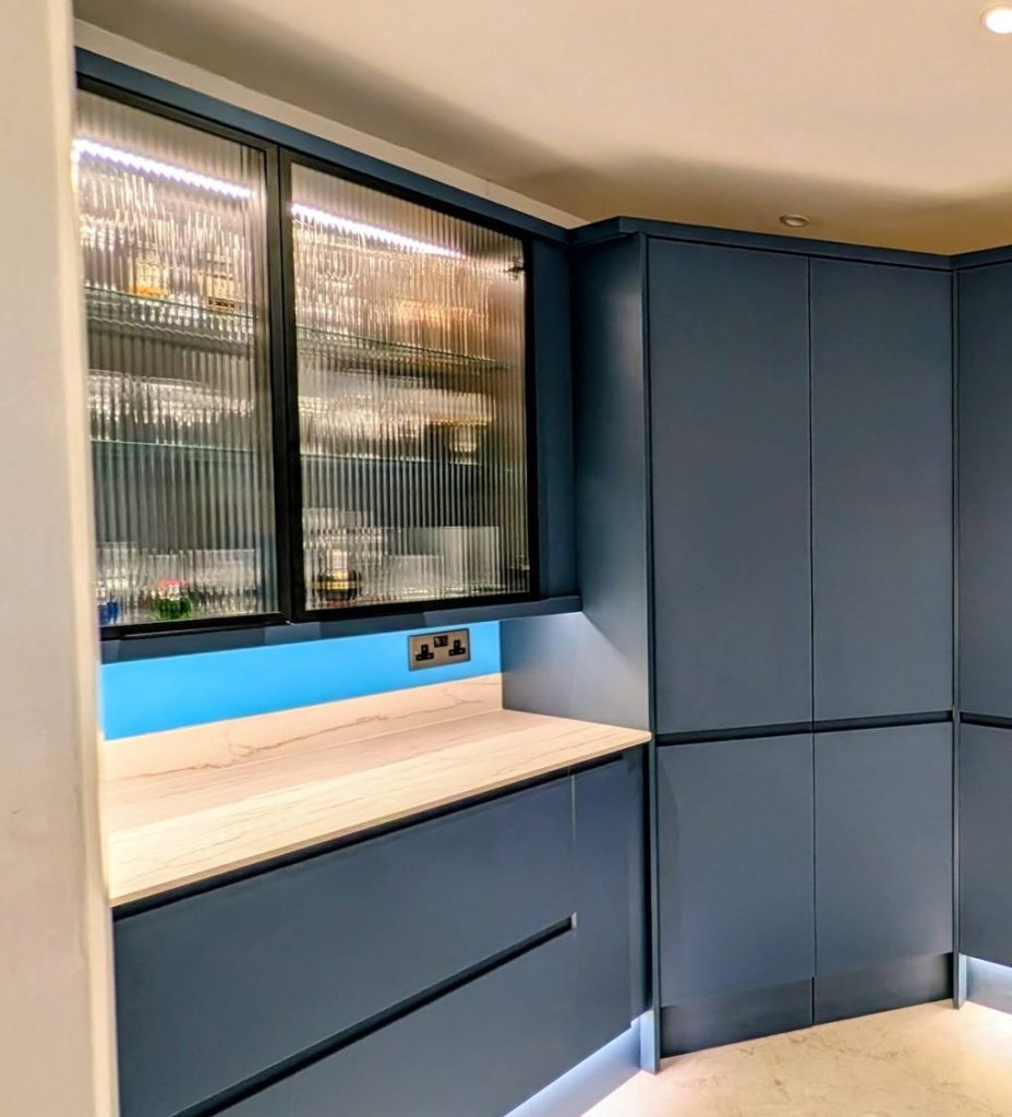Blue handleless kitchen with white worktops and a corner larder and fluted glass vitrine