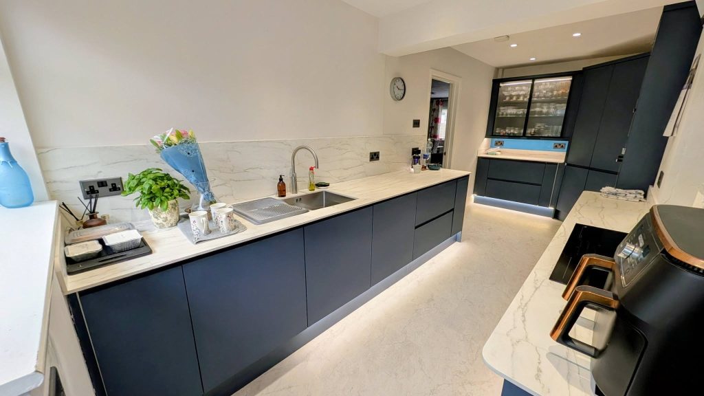 Blue handleless kitchen with white worktops and a sink run on the left side and a glazed wall unit at the back