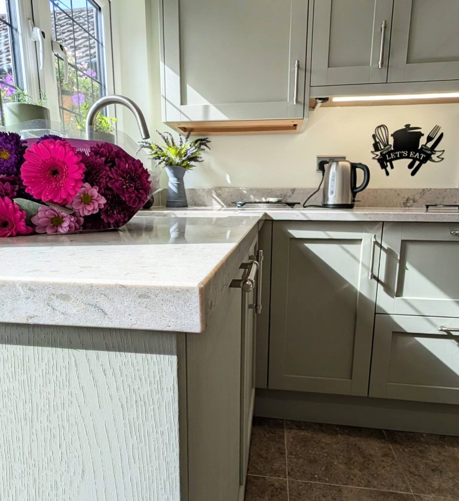 Detail of taupe-green Shaker kitchen with Quartz worktops, stainless steel handles and tap