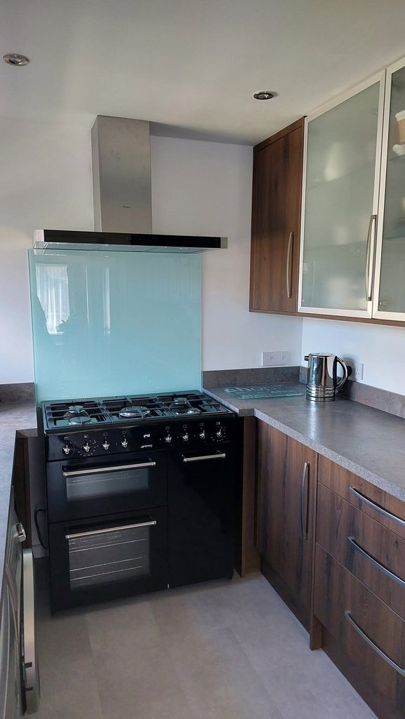 Detail photo of a far end of the galley layout kitchen with a freestanding black gas range cooker at the end. Sleek brushed steel handles mating those original ones on the glass wall cabinets.
